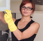 Young woman wearing rubber, yellow gloves cleaning a cupboard. She has stopped to look at the camera.